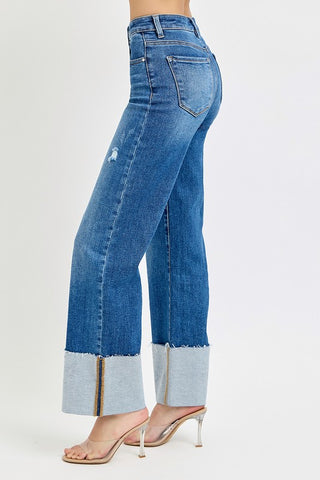 A woman wearing high waisted dark blue wide leg jeans with a big cuff paired with boots and a sweater. 