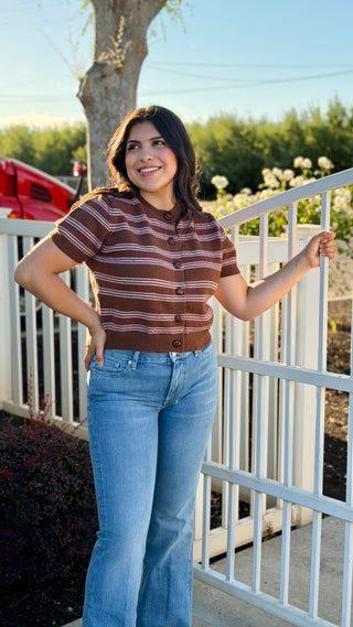 A woman wearing a brown sweater with pink and teal stripes. 