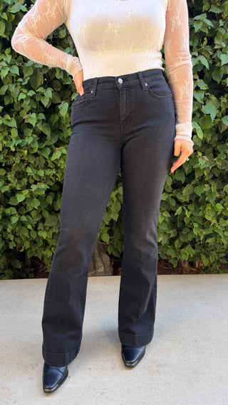 Person wearing black jeans and a beige top against a green leafy background