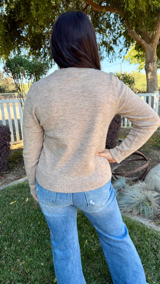 A woman wearing a long sleeve beige sweater with blue jeans outdoors.