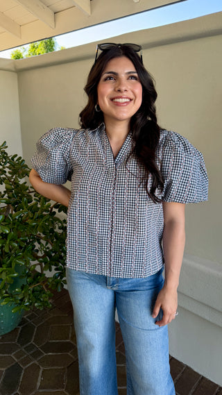 A woman wearing a black plaid blouse with jeans.
