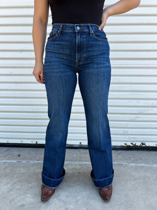 A woman wearing high - waisted jeans with dark blue 7 stitching on the back pocket. 