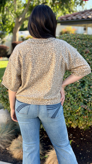 Woman wearing a neutral leopard print ribbed knit short sleeve top with a crew neckline, rolled sleeves, and a slightly cropped fit paired with medium wash jeans.