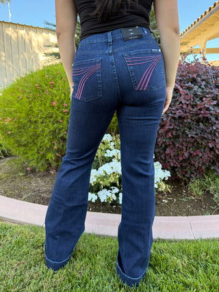 Person wearing blue jeans with decorative stitching in a garden setting