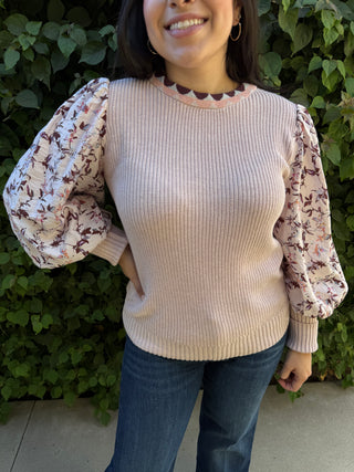 A woman wearing a pink knitted sweater with a floral print on the sleeves. 
