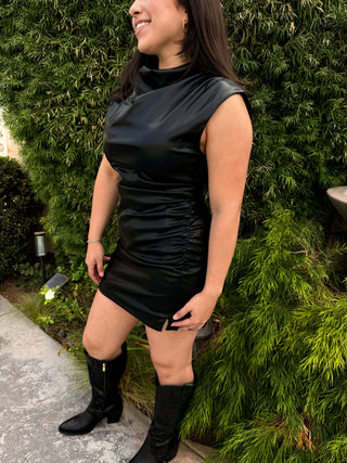 A woman wearing a sleeveless, high-neck, ruffled faux leather dress with a large zipper at the back. 