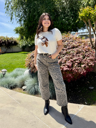 Woman wearing a cream short-sleeve sweater with a horse graphic, paired with leopard-print pants.
