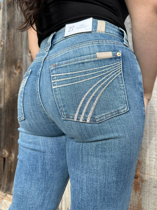 A woman wearing light wash denim trousers with a cream 7 stitched on the back pocket. 