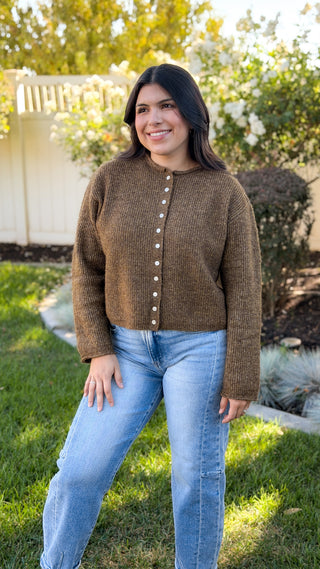 Full-length outdoor view of olive brown button front cardigan sweater styled with light wash jeans
