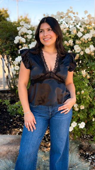Woman wearing a black satin V-neck top and wide-leg jeans outdoors, full-length front view