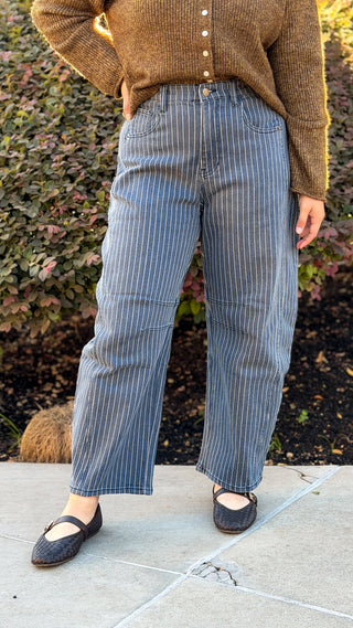 Front view of pinstripe denim high rise barrel jeans with a curved leg and cropped ankle, worn with black Mary Jane flats
