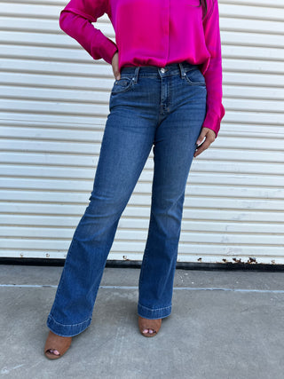 A woman wearing medium wash blue jeans with a blue 7 stitching on the back pocket. 
