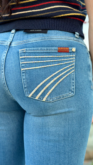 Close-up back view of a person wearing light blue denim jeans with distinctive contrast stitching on the back pocket and a striped sweater at the top.