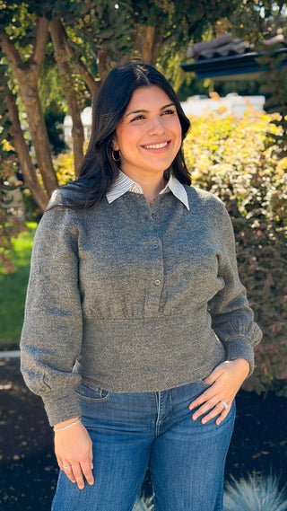 Woman wearing a gray bubble sleeve sweater top with a white contrast collar and blue jeans outdoors
