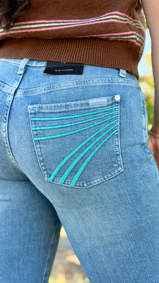 A woman wearing light blue jeans with turquoise embroidery on the back pockets, paired with a brown striped top.