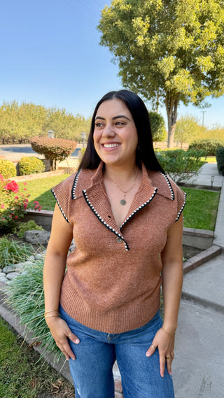 Woman wearing a brown sleeveless sweater with decorative black and white trim.