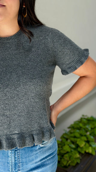 Close-up of charcoal gray knit sweater top showing the ruffle sleeve trim and ruffle hem detail