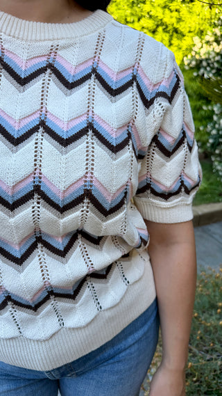 Person wearing a short-sleeve sweater with a zigzag pattern in an outdoor setting