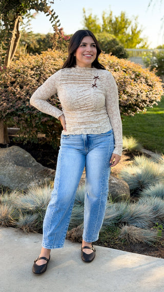 Woman wearing Risen high rise barrel jeans in light wash with a beige lace top and black flats, full outfit view