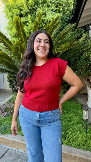 Woman wearing a cherry red cap sleeve knit sweater top with a ribbed hem.