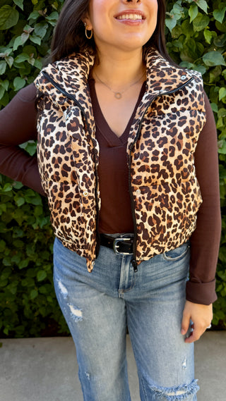 Person wearing a leopard print vest over a brown shirt with blue jeans, 