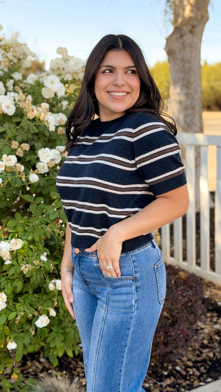 Model smiling in navy striped crew neck sweater top and jeans outdoors