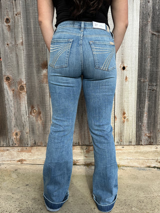 A woman wearing light wash denim trousers with a cream 7 stitched on the back pocket. 