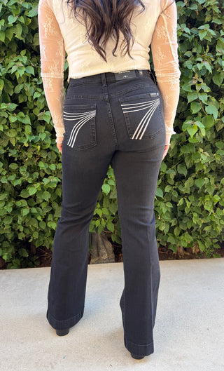 A woman wearing black flared jeans with white stitching