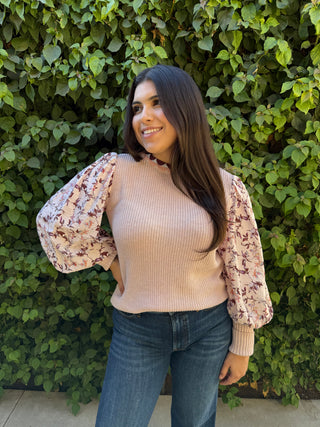 A woman wearing a pink knitted sweater with a floral print on the sleeves. 