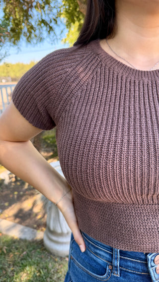 Woman wearing a brown top knitted top with a satin tie on the back and blue jeans.