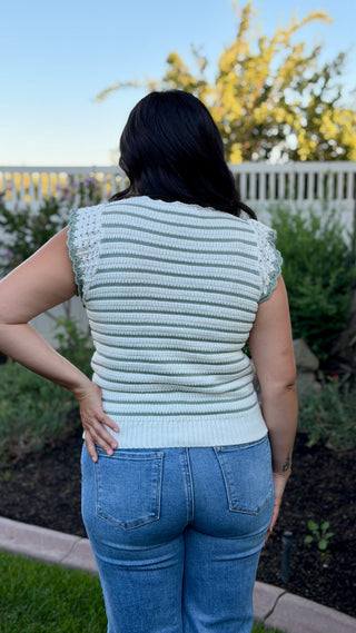 Woman wearing a white and sage striped sleeveless crocheted knit top.