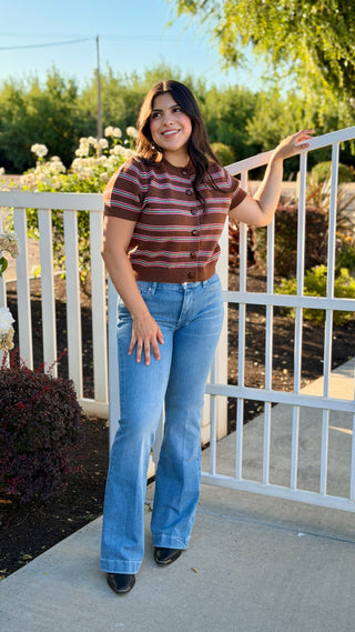 A woman wearing a brown sweater with pink and teal stripes. 