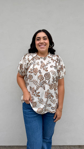 Woman wearing a floral blouse and jeans against a plain background