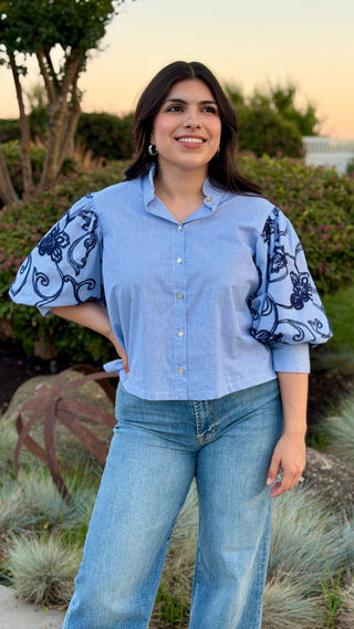 Woman wearing a button up in light blue shirt with patterned sleeves.