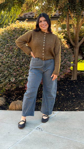 Full-length outdoor view of blue and white pinstripe barrel jeans styled with a brown knit cardigan and black flats