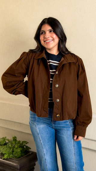 Woman wearing a brown cropped bomber jacket with a high stand collar over a striped tee and light-wash jeans