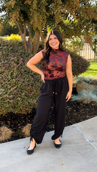 Full-length outdoor view of burgundy floral print mock neck top styled with black wide leg pants and black heels