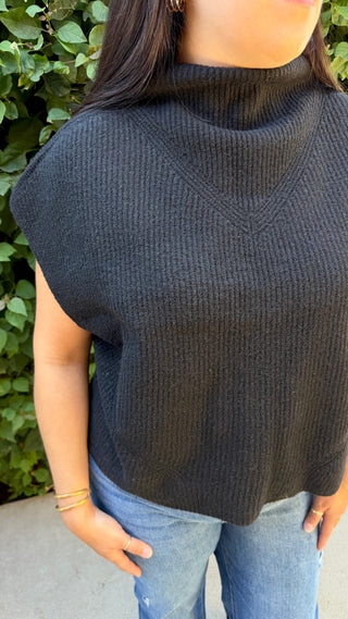 Woman wearing a black knitted sweater vest and blue jeans.