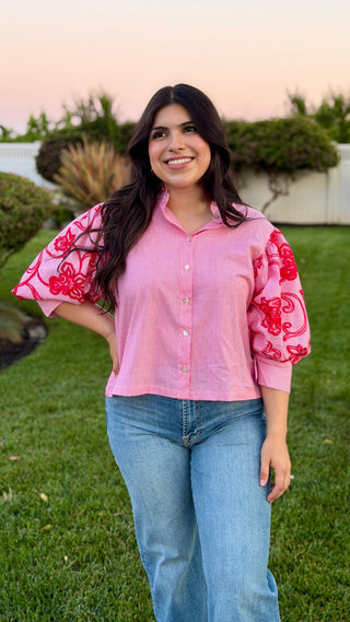 Woman wearing a red blouse with red embroidery standing outdoors.