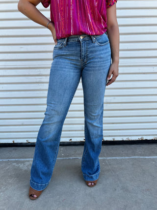 A woman wearing light-wash, mid-rise denim jeans showing the back pocket detail.