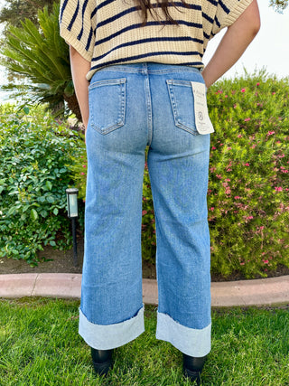 A woman wearing high-waisted cuffed wide-leg jeans in a medium wash and black boots.