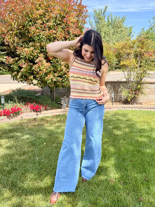 A woman wearing high waisted jeans that are a medium wash with a raw hem and are a wide leg style. 