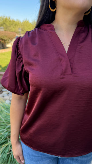 woman wearing a burgundy blouse with ruffled sleeves.