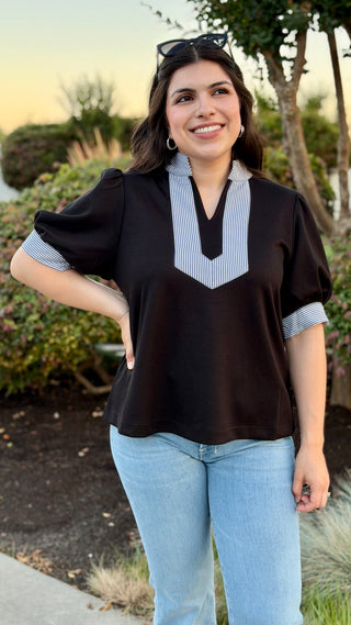 Woman wearing a black blouse with a white collar.