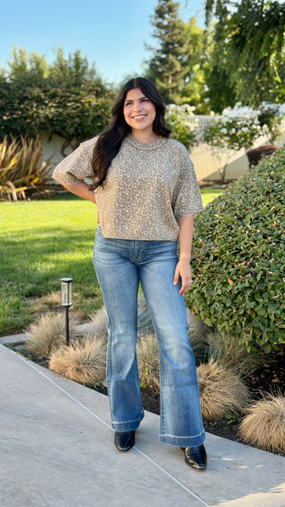 Woman wearing a neutral leopard print ribbed knit short sleeve top with a crew neckline, rolled sleeves, and a slightly cropped fit paired with medium wash jeans.