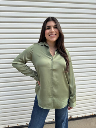 A woman wearing a green long sleeve button-down shirt and blue jeans.