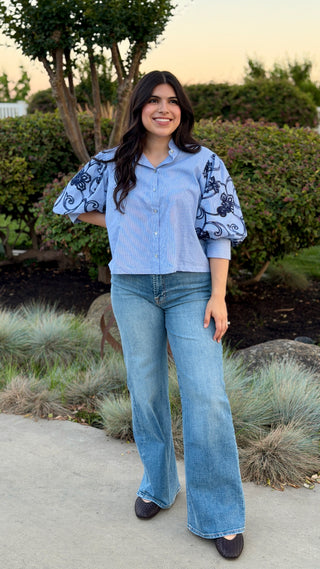 Woman wearing a button up in light blue shirt with patterned sleeves.