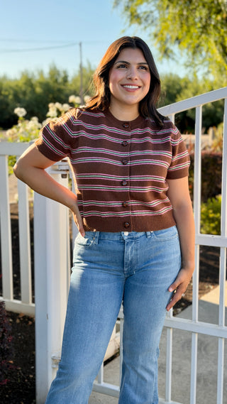 A woman wearing a brown sweater with pink and teal stripes. 
