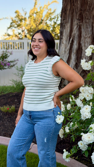 Woman wearing a white and sage striped sleeveless crocheted knit top.