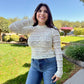 Woman wearing a light sweater and jeans standing outdoors on a sunny day.